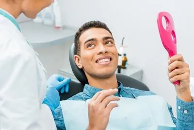patient smiling while holding up a mirror after his laser dentistry procedure at Lynn Dental Care in Dallas, TX